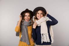 两个美丽的女人戴帽子和围巾的图像微笑着对相机在灰色背景隔离