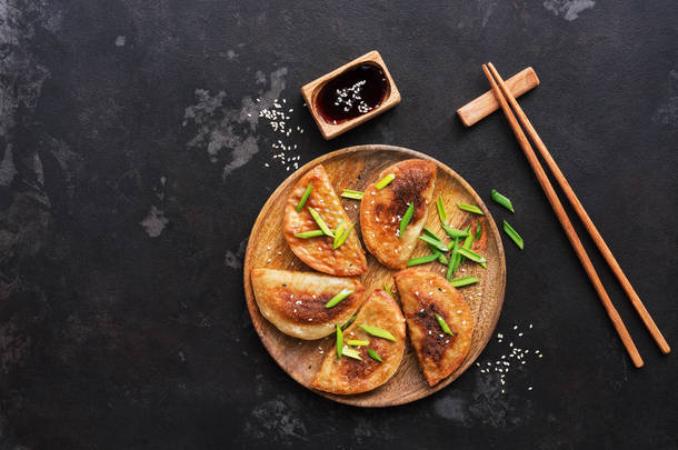 自制的亚洲油炸饺子与香葱, 酱油和筷子在黑色的石头背景。韩国日本料理。顶部视图, 文本空间.