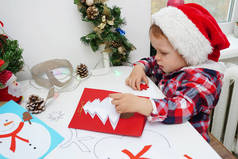 戴着圣诞礼帽的小女孩用彩色圣诞纸制了一张卡片。冬季孩子创造力的概念