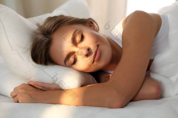 美丽的年轻女子，睡觉时<strong>躺</strong>在<strong>床</strong>上舒舒服服地和幸福。她脸上的阳光黎明