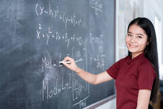 美丽的亚洲学生写在黑板上用粉笔在课堂上.