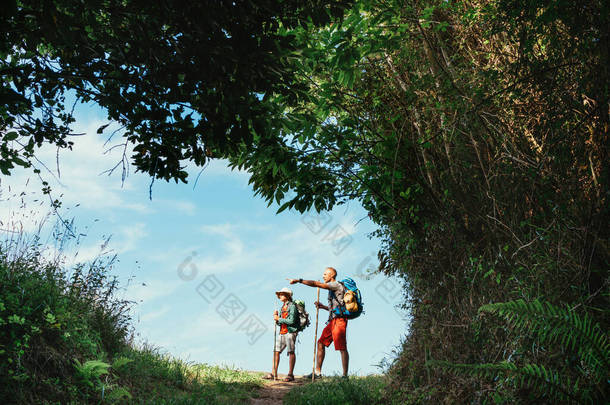 父亲和儿子的背包客在森林小径上徒步旅行，稍作休息。与孩子一起旅行的<strong>快乐</strong>父母的概念形象.