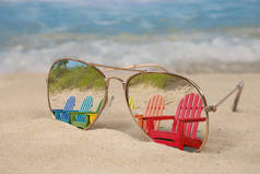 五颜六色的一排阿迪朗达克椅子反映在海滩沙滩上的飞行员太阳镜