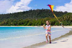 在热带海滩上带着五颜六色的风筝奔跑的孩子。孩子放飞彩虹风筝。小女孩在海滨玩玩具飞机。家庭暑假在异国情调的海岛。水和沙子乐趣为孩子. 