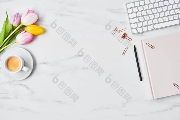 办公桌与电脑, 粉红色和黄色的郁金香, 咖啡杯和粉红色的日记在白色大理石背景。平躺着。复制<strong>文本</strong>的空间。顶视图.
