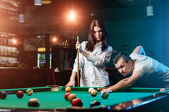 一个男人和一个漂亮的女孩在打台球, 一个男人在教一个女孩打台球。黑暗的背景。愉快的消遣, 家庭休息, 娱乐, 假日.