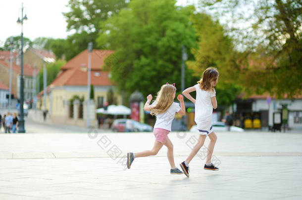 在一个美丽的夏日,两个可爱的妹妹在一个城市玩得很开心.有孩子的积极的家庭休闲。户外家庭娱乐.