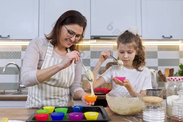 妈妈和女儿在家里厨房一起做松饼.将生面团倒入硅胶模中的母子.母亲节、家庭、自制<strong>烘焙</strong>健康<strong>食品</strong>