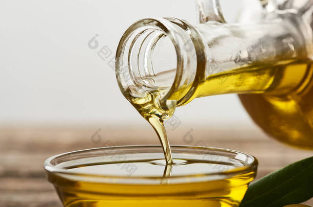 将橄榄油从瓶子倒进灰色背景的玻璃碗中