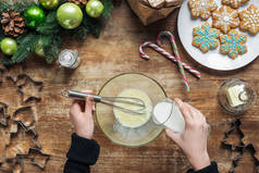 妇女将牛奶倒进碗里, 同时在带有装饰花圈的木桌面上做圣诞饼干的裁剪镜头