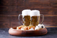 两个杯子啤酒和热狗放在木制底盘上的图片