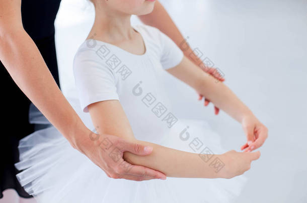 芭蕾舞老师在古典舞蹈学校帮助小芭蕾舞演员. 女舞蹈教练正在教小女孩用手做舞蹈姿势。 为孩子们练习。 靠近点.