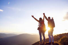 在夏天的一次徒步旅行中，一对快乐的男女在日落时分在山顶上观光