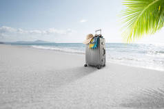 在热带海滩上可以看到灰色手提箱和帽子 
