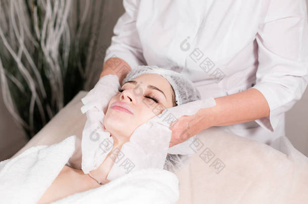 用消毒过的餐巾擦拭脸.年轻漂亮的女人在<strong>美容院</strong>接受治疗。使用洗脸泡沫.