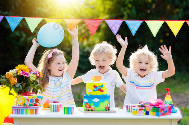孩子们在生日蛋糕上吹蜡烛。孩子聚会装饰和食物。男孩和女孩庆祝小弟弟的生日。交通和汽车儿童事件的主题。带礼物和糖果的孩子.
