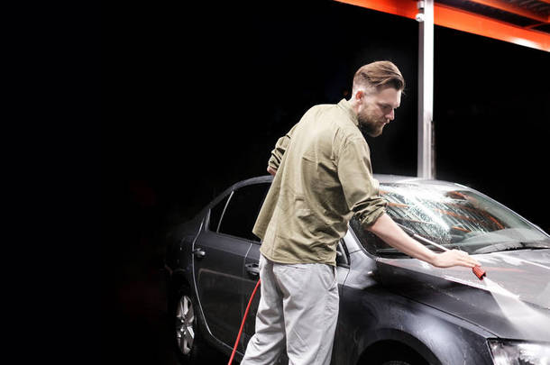有胡子或洗车的人晚上在洗车时用高压器具洗一辆灰色的汽车。