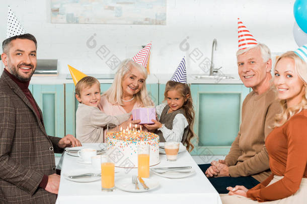 快乐的孩子们坐在祖母的身边，和家人一起坐在生日蛋糕旁边