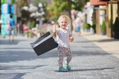 可爱的小宝贝女孩站立或行走在水口村街道中间期间销售提着购物袋黑色，在她手中，人群拥挤的背景