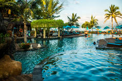 海滩日光浴附近的游泳池在热带度假胜地与棕榈在日落期间, 吉利特拉温干, 龙目岛, 印度尼西亚