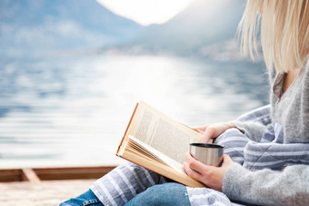 女孩正在海边的木码头上看书，冬天的大海，山，海滩。舒适的野餐，有热热的热蒸饮料，茶，咖啡或可可在热水瓶，温暖的格子。享受生活、放松的理念.图片