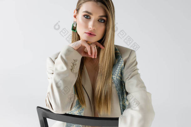 穿着西服的年轻女子坐在木椅上，看着白色的照相机