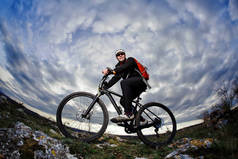 对美丽的蓝天白云，晚上骑自行车在岩石上的黑色运动服的自行车手.