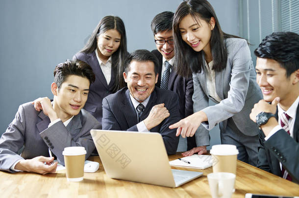 一支由亚洲企业高管组成的团队, 使用膝上型电脑在办公室工作, 快乐和微笑.