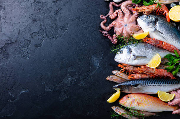 新鲜生鱼和海鲜在黑色板岩背景的分类。顶部视图。复制空间.