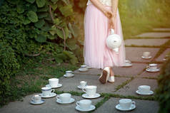 爱丽丝在仙境。一个穿着长裙、手里拿着茶壶的姑娘，手里拿着一套茶杯和茶托.