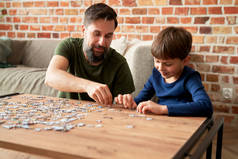 男孩在家里客厅里和父亲一起解开拼图                               