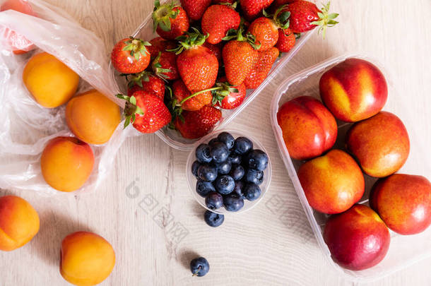 用蓝莓、<strong>草莓</strong>、油桃和桃子在木制表面的塑料容器中的<strong>水果组合</strong>的顶部视图