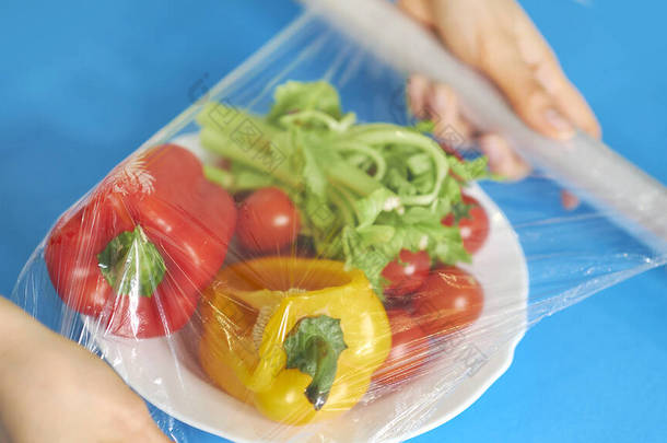 女人用食品膜把食物贮存在白桌上.包装产品用透明聚乙烯食品膜辊.