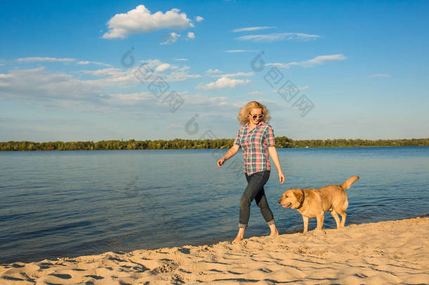 幸福的年轻女人，漫步在沙滩上与她的金毛在夕阳的<strong>余晖</strong>