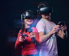 愉快的朋友玩视频游戏佩戴虚拟现实眼镜与控制器。在深色背景下隔离.