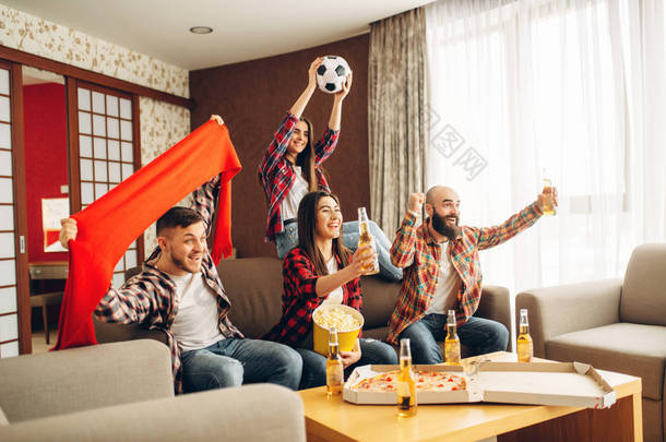 微笑的朋友为他们最喜爱的球队，足球迷欢呼。一群人在家里播报电视。快乐的公司庆祝目标