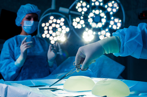 护士手外科医生在背景运行病人组采取外科手术器械。隆胸