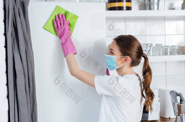 戴着医疗面罩和橡胶手套的妇女在清扫冰箱时拿着破布 