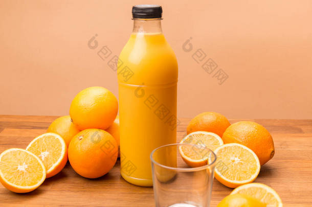 橙汁，橙子切成两半，透明的瓶子，瓶盖上装有新鲜榨过的橙汁，木制表面有透明的空杯子