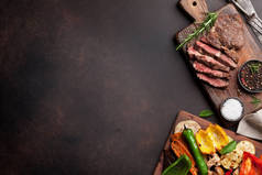 烤的蔬菜和牛肉牛排在木制的桌子上砧板上。顶视图与副本空间