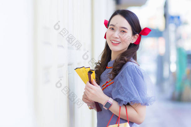 一名身穿蓝灰色旗袍的年轻亚洲妇女，在一个白色木门旁边拿着一个布袋，门的背景是城市.