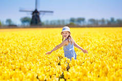 孩子在郁金香花卉领域与风车在荷兰。小荷兰女孩在白色帽子与弓采摘花为花束。孩子在郁金香领域在荷兰在风磨房.