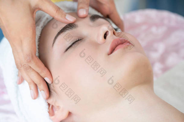 在一个豪华温泉度假胜地，放松了的妇女躺在温泉床上接受按摩治疗师的面部和头部按摩治疗。健康、减轻压力和恢复活力的概念.