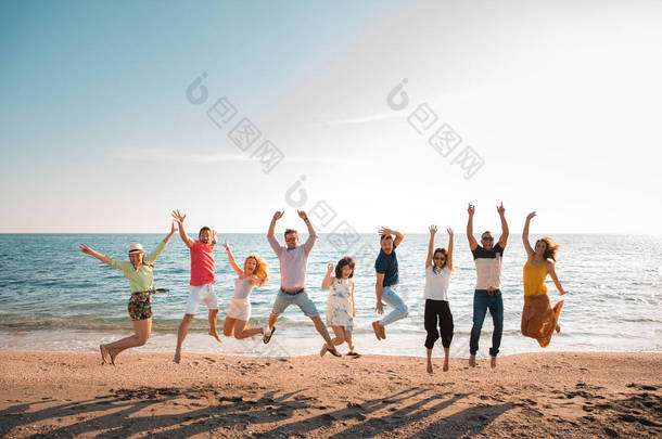 一群快乐的年轻人跳在<strong>海滩</strong>上美丽的<strong>夏日</strong>日落。九人, 五名妇女和四人。朋友和假日概念 