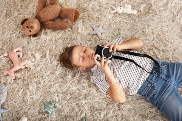 可爱的小摄影师与专业相机躺在地毯上