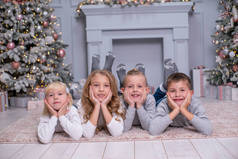 两个男孩和两个女孩躺在地毯上，在一间装饰着圣诞装潢的房间里笑着。彼此相爱.