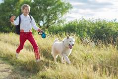 带着狗在大自然中散步的女孩，带着宠物在阳光灿烂的草地上奔跑的孩子