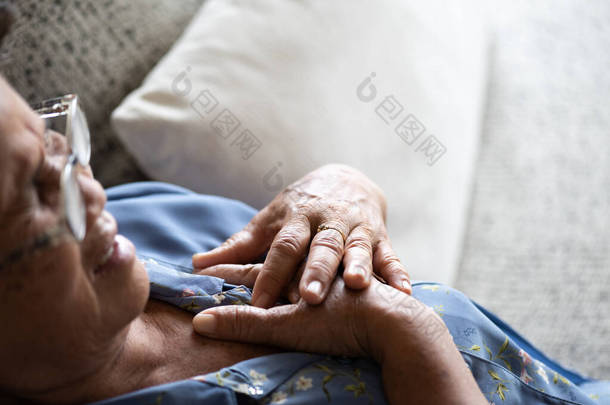 生病的亚洲老妇人躺在沙发上，心痛，在家里心脏病发作。高级保健概念.