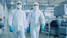 两名工程师/科学家在危险品无菌西装步行通过技术先进的工厂/实验室。用 Cnc 机械清洁高科技环境.
