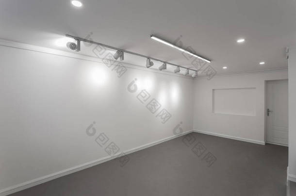 画廊房间里没有镜框的空白白墙。为艺术展览提供了明亮的空间。画廊照明，聚光灯没有人。设有深灰色自平整地面的展览厅. 